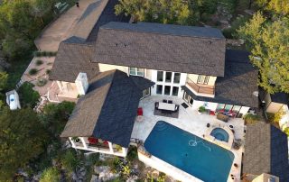 Aerial view of a modern house with a backyard patio, swimming pool, outdoor furniture, and surrounding trees.