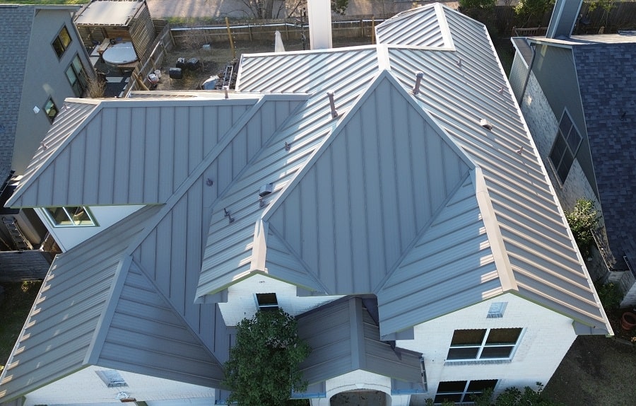 Aerial view of a house with a gray metal standing seam roof, featuring multiple peaks and sections.
